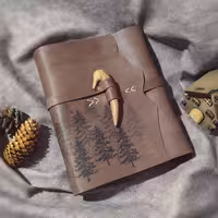 کلاسور چرمی کوهستان کاج، 21 در 16 ، چرم بزی خاکی رنگ، همراه صد برگ کاغذ نخودی خطدار، حک جنگل کاج، همراه بست شاخ چوب بلوط