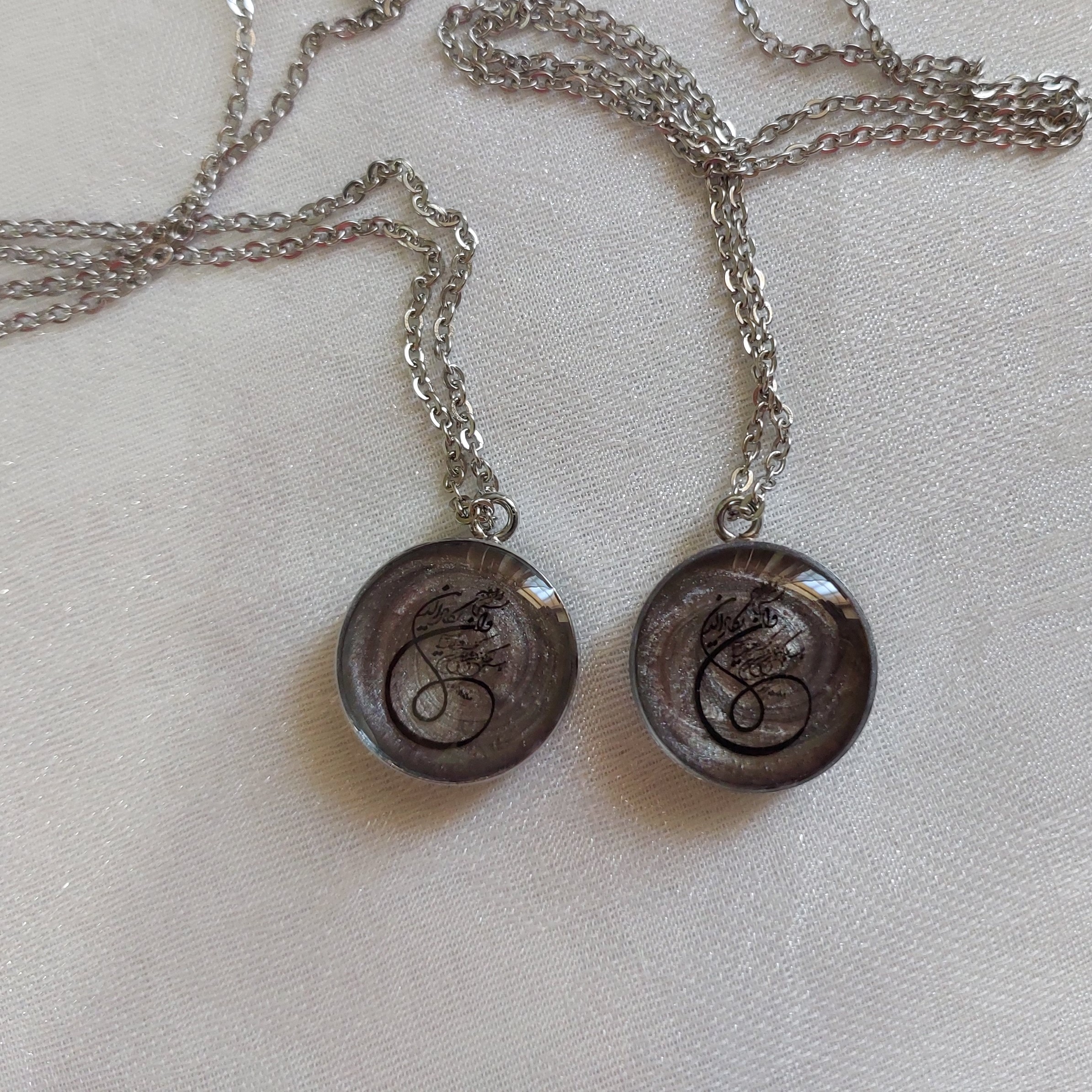 گردنبند رزینی دو طرف کار شده مزین به وان یکاد و حرز امام جواد(ع) قاب استیل نقره ای و یراق آلات رنگ ثابت 