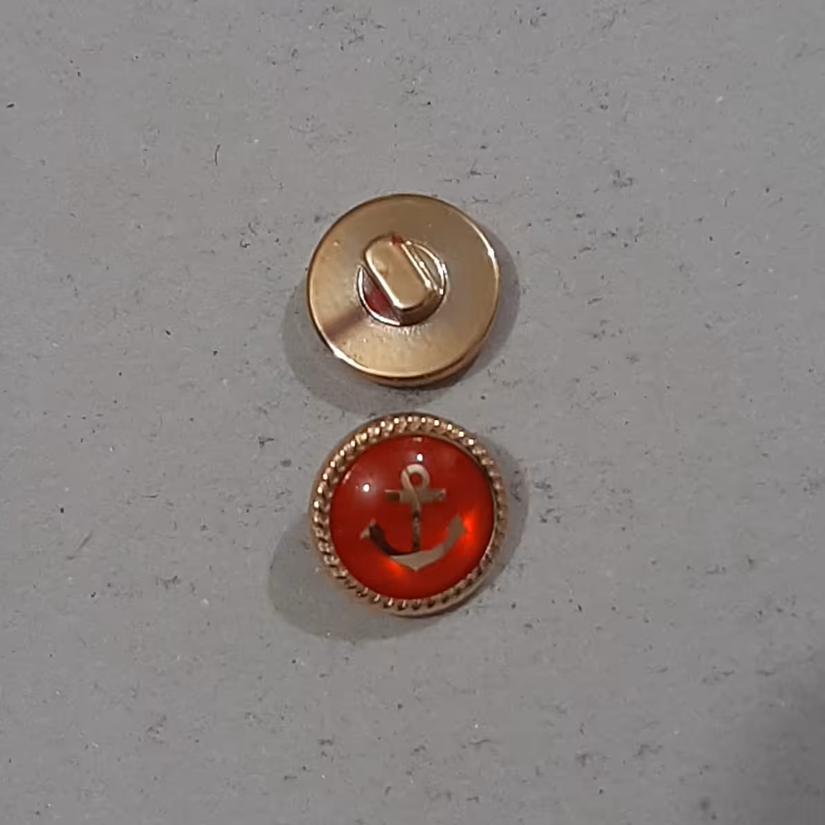 دکمه قرمز  طلایی . طرح لنگر . یک سانت و هفت میل. دور فلزی طلایی