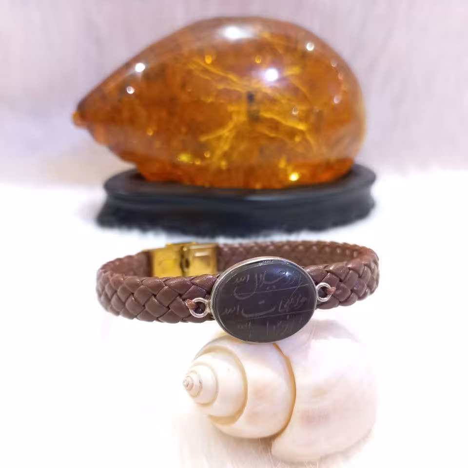 دستبند چرم حصیری با نگین حدید طبیعی و حکاکی ذکر هفت جلاله داخل قاب نقره دستساز