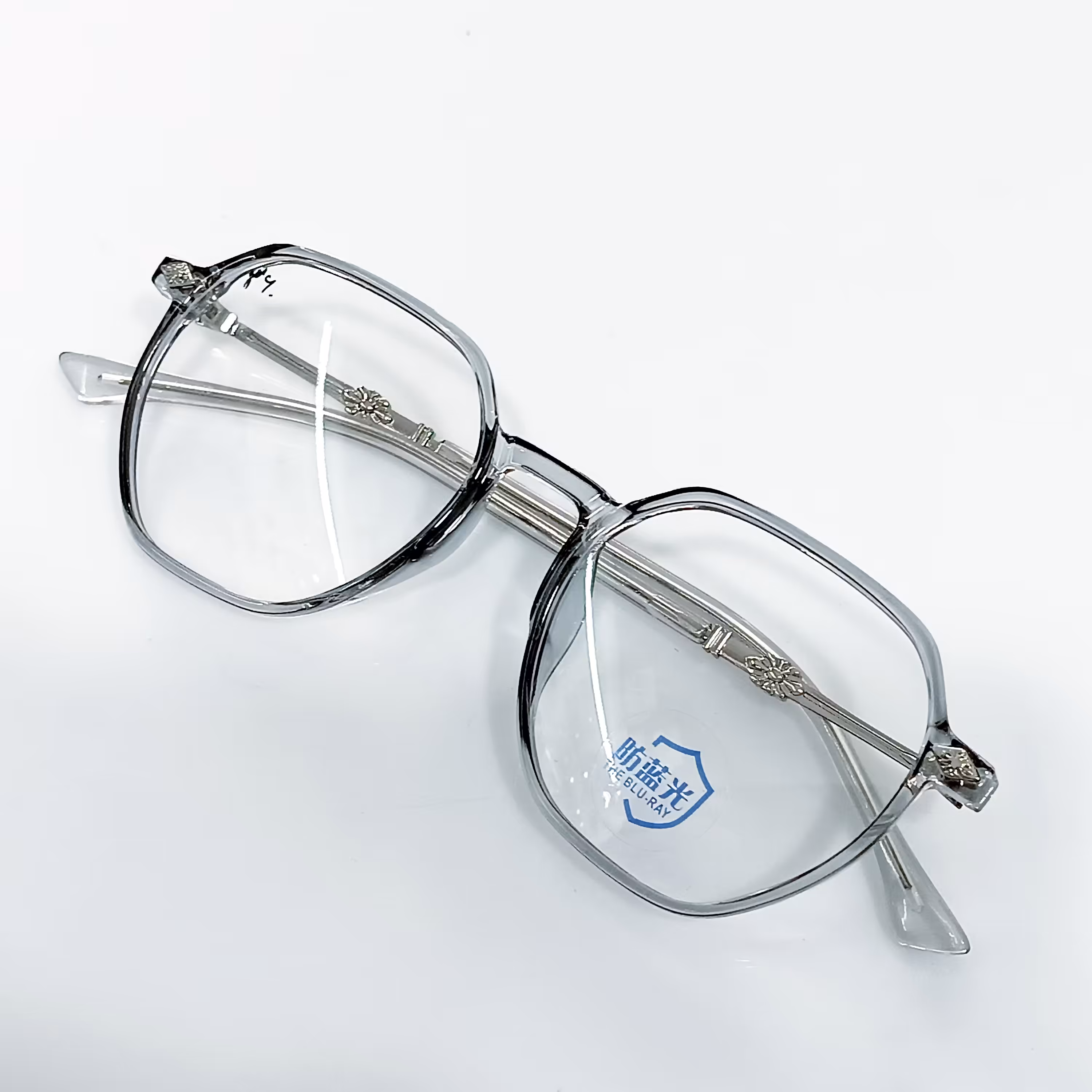 عینک طبی چند ضلعی رنگ طوسی نوک مدادی دسته فلز نقره ای با عدسی سفید دیر خش پذیر نمره اختصاصی همراه با جلد و دستمال 