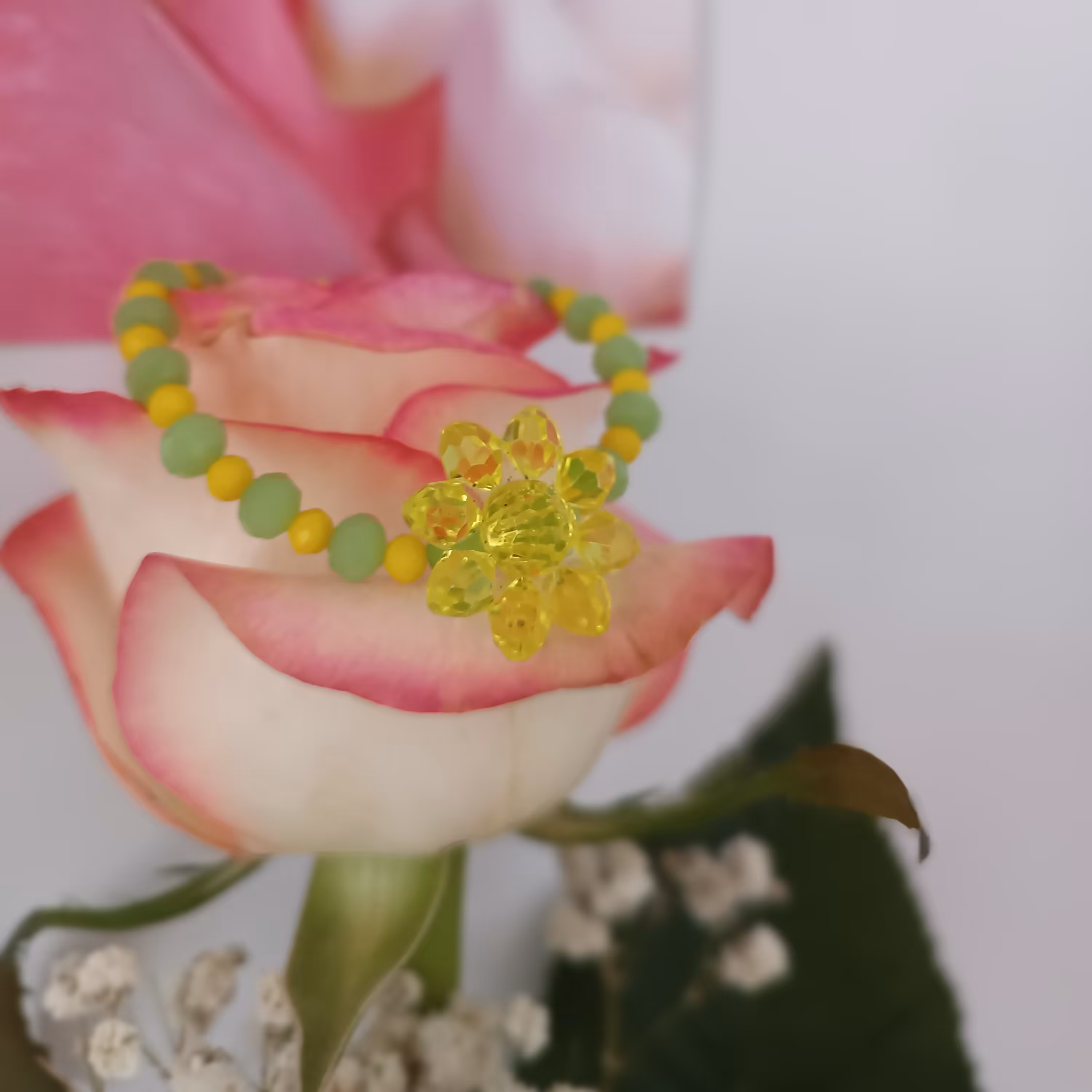 دستبند با پلاک گل که رکن پلاک گل زرد هستش و با مروارید زرد و سبز هستش 