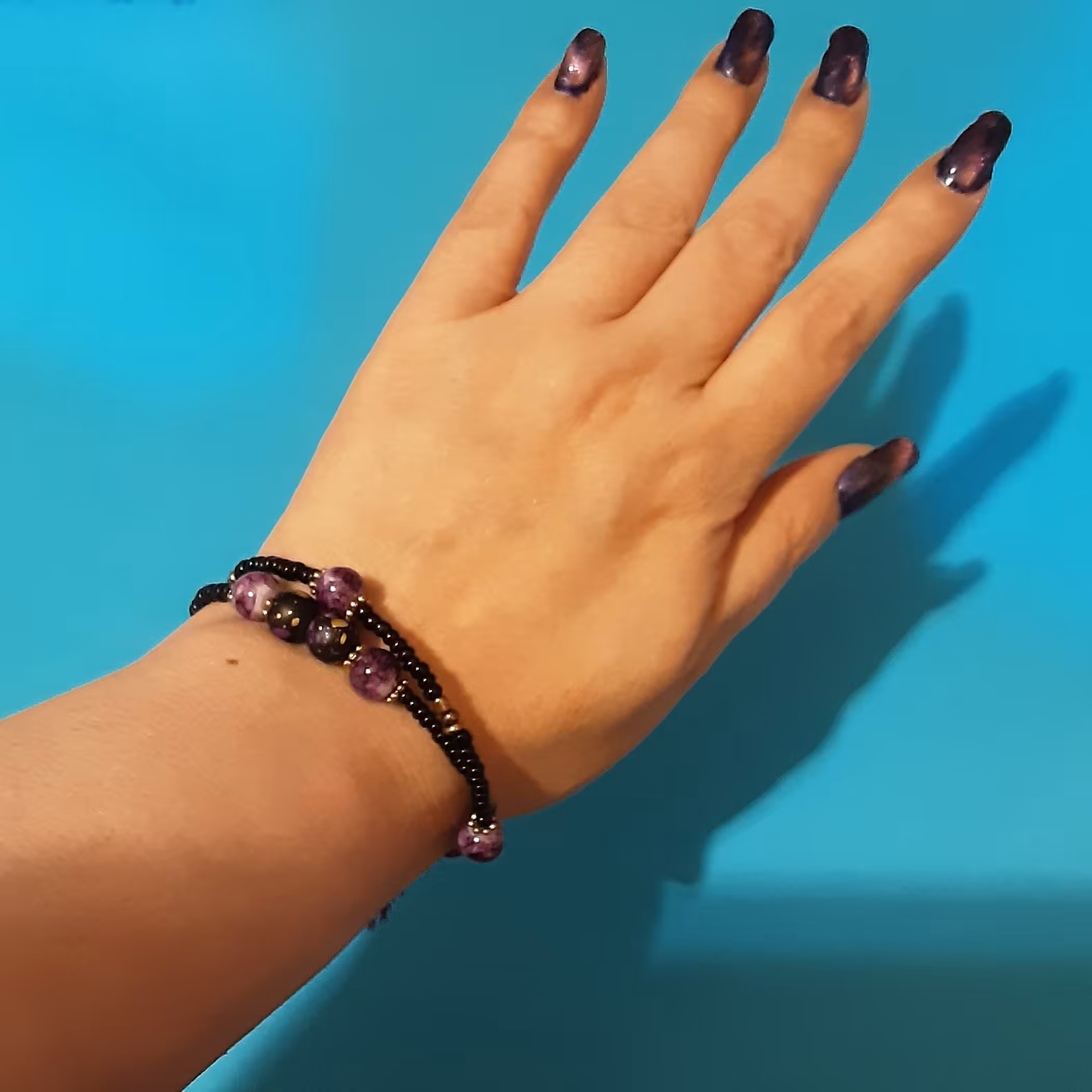 دستبند منگوله دار.2 دور.دارای سنگهای مشکی و دانه های برنزی به همراه سنگهای بنفش رگه دار مدل آمیتیست.فری سایز