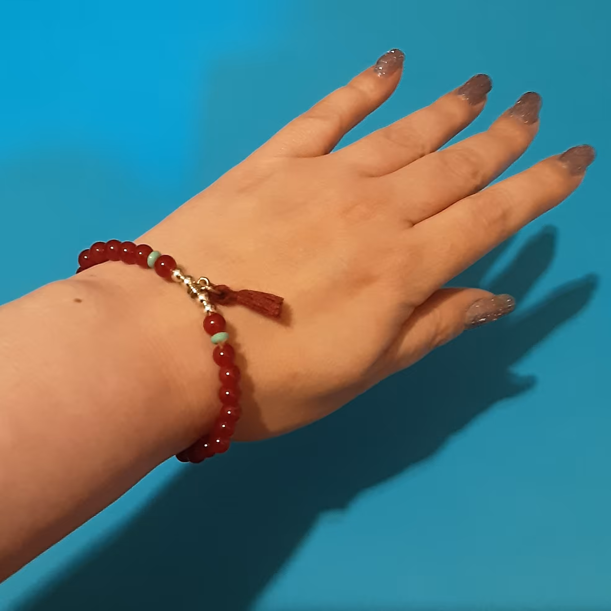 دستبندکشی منگوله دار.کار شده با سنگهای قرمز اناری وگوی های استیل به همراه 2 سنگ لپه ای فیروزه ای و منگوله قرمز