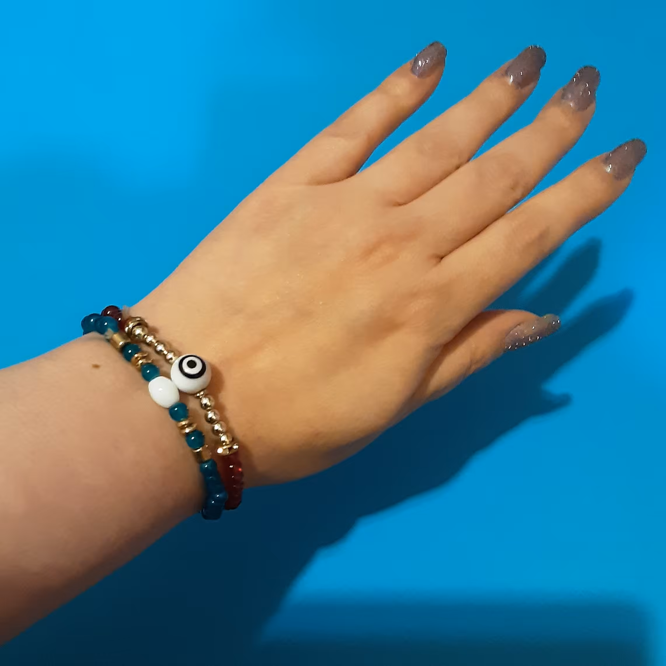 دستبند کشی.یک جفت.مدل چشم نظر.کارشده با سنگهای قرمز اناری و فیروزه ای تیره به همراه رینگها و مرواریدهای استیل