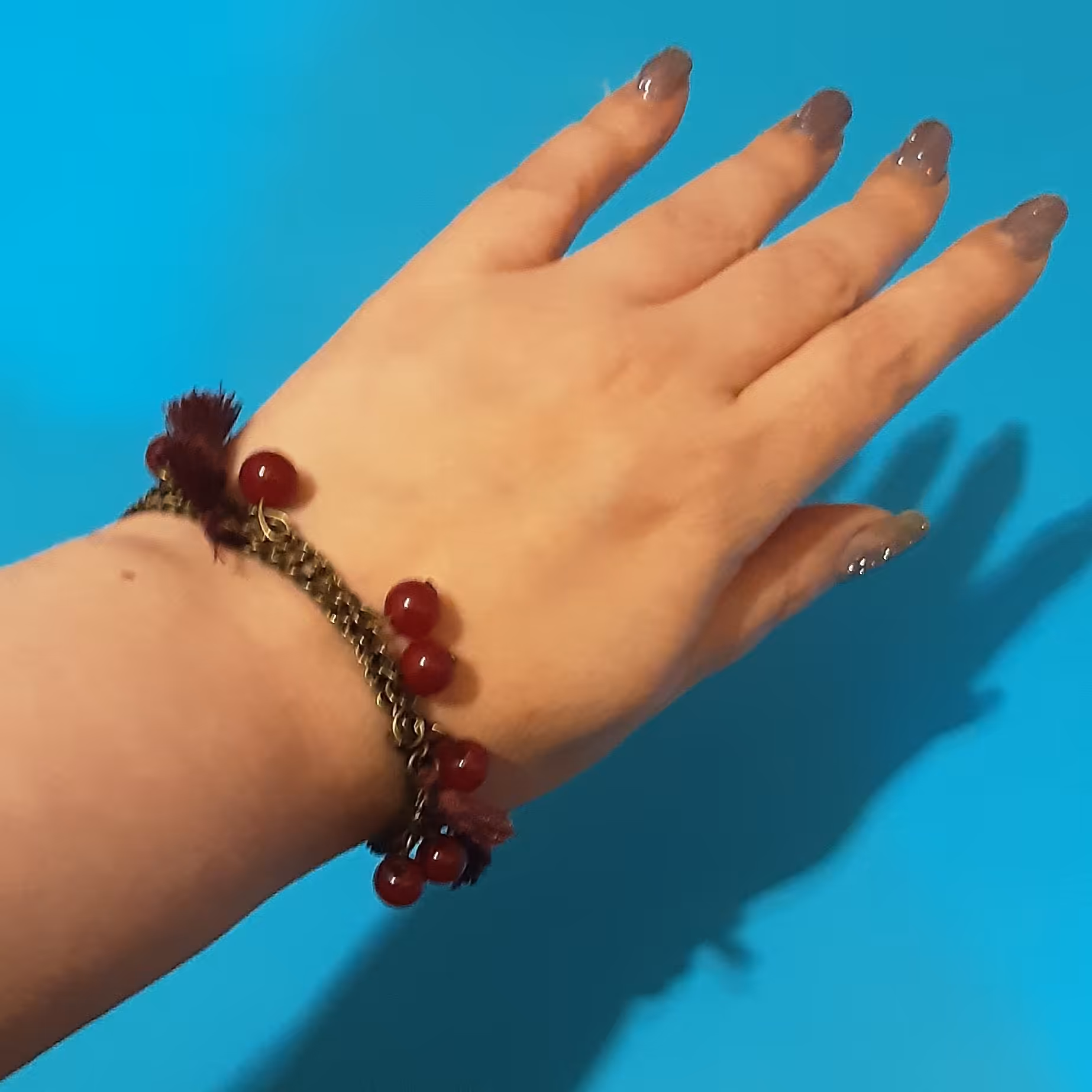 دستبند آویز و منگوله دار.دارای 3 رج زنجیربرنزی به همراه آویزهایی از سنگ جید قرمز و منگوله.قابل سایز