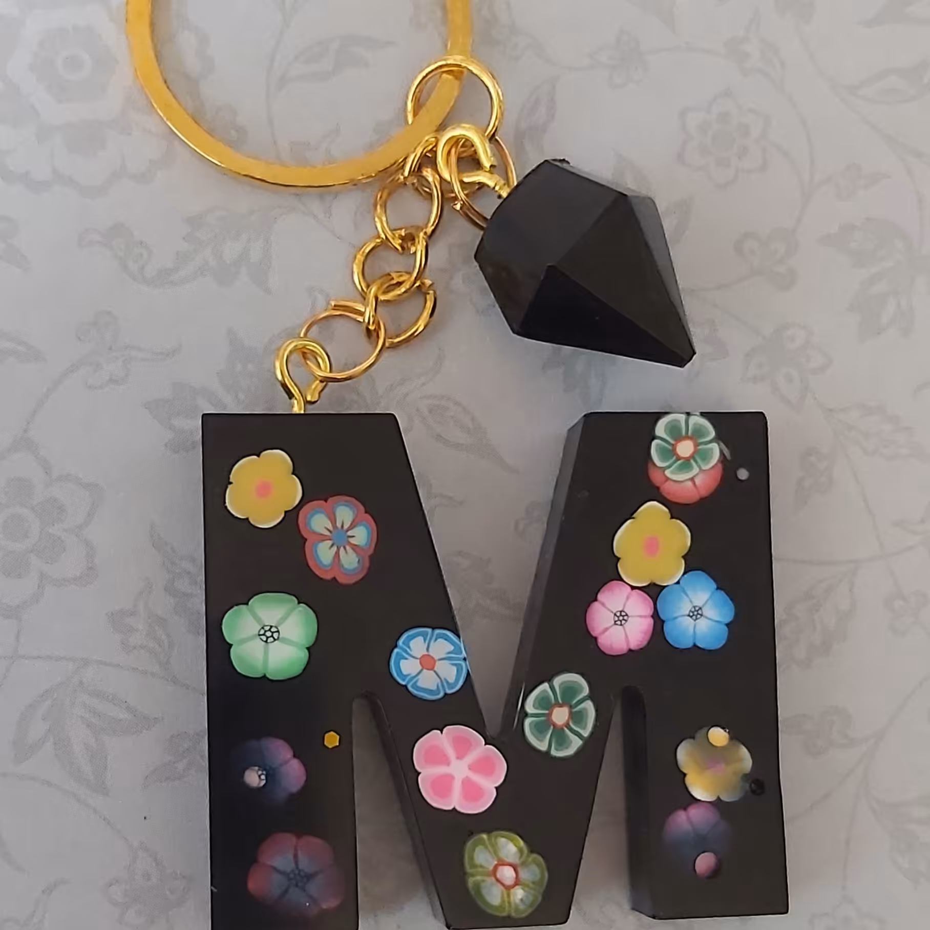 جاکلیدی رزینی حرف Mمشکی گلدار بااویزالماس یک عدد