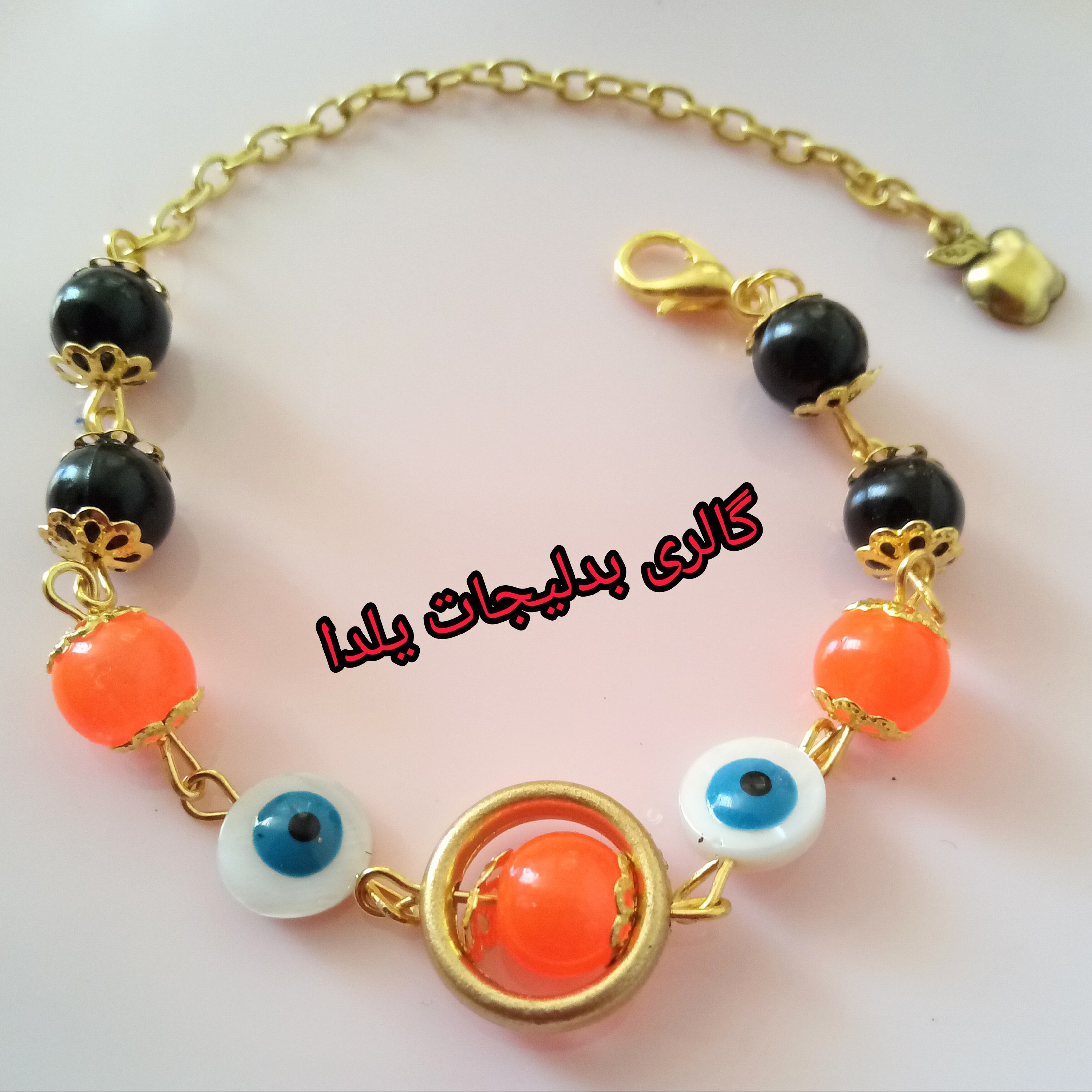 بدلیجات دستبند چشم نظر و تزئین شده با مهره های سنگی نارنجی ومروارید های مشکی واویز سیب طلایی 