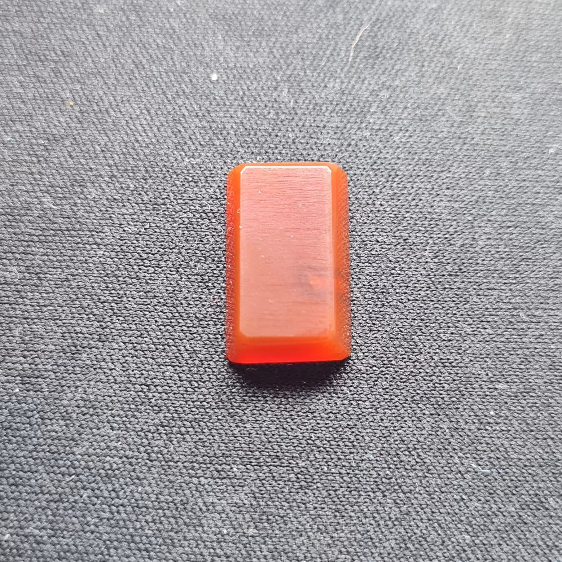 نگین عقیق قرمز (مشخصات: طول: 1.8 سانتی متر. عرض: 1.1 سانتی متر. ارتفاع: 0.4 سانتی متر.)