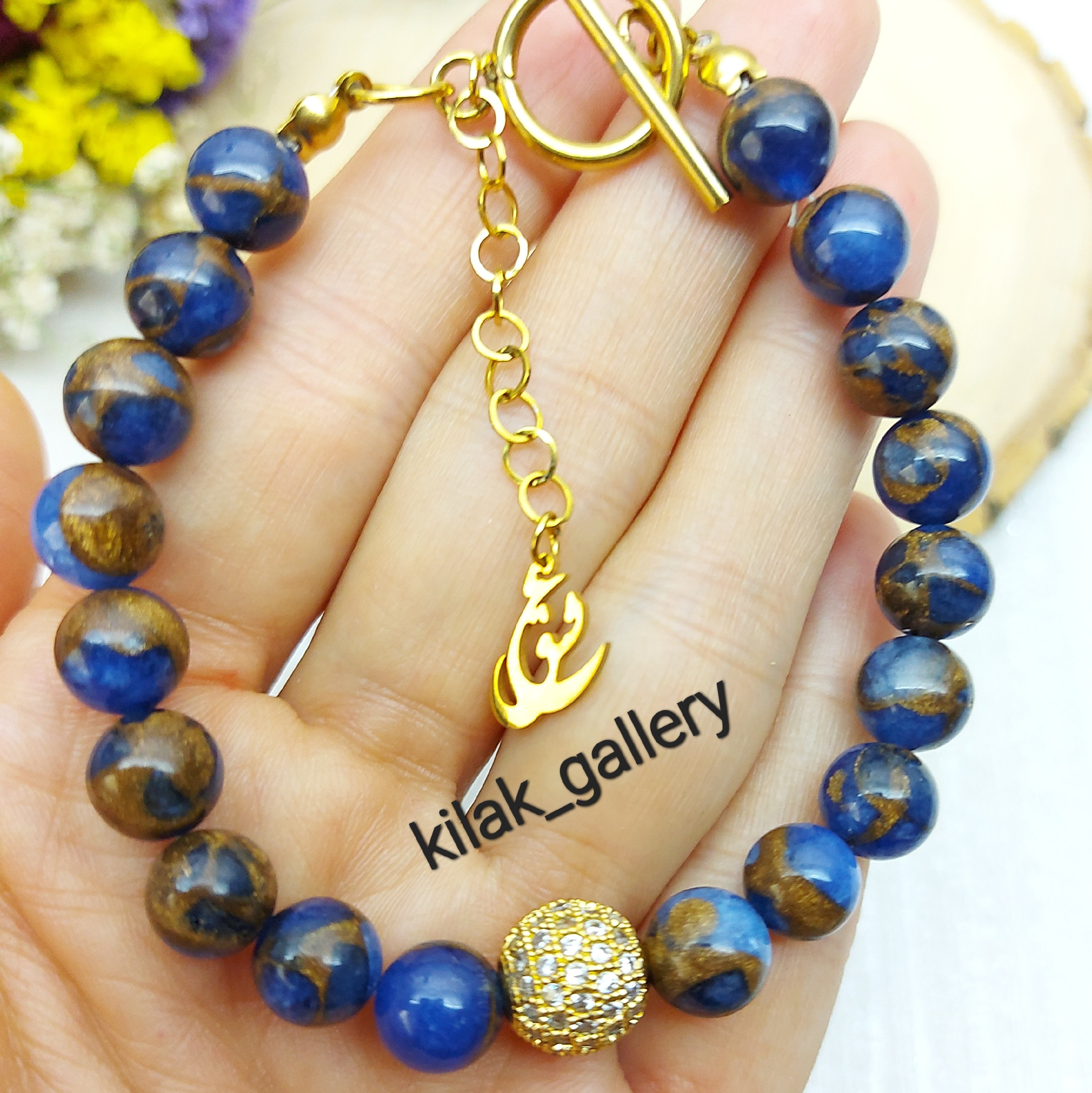 دستبند سنگی با سنگ عقیق شجر آبی کاربنی با رگه های طلایی با اویز و قفل استیل تی و گوی سوارسکی 