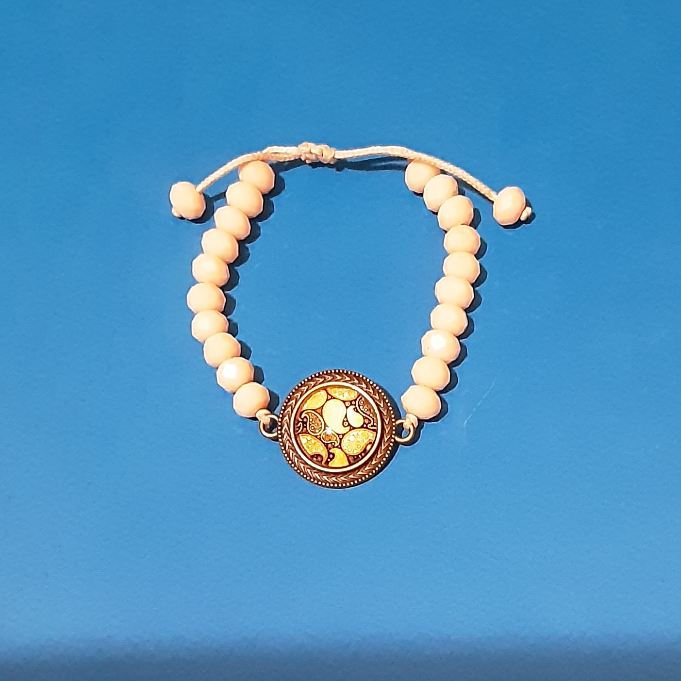 دستبند بافت با سنگهای سفید مایل به کرم روشن به همراه پلاک برنزی طرح بته جقه.