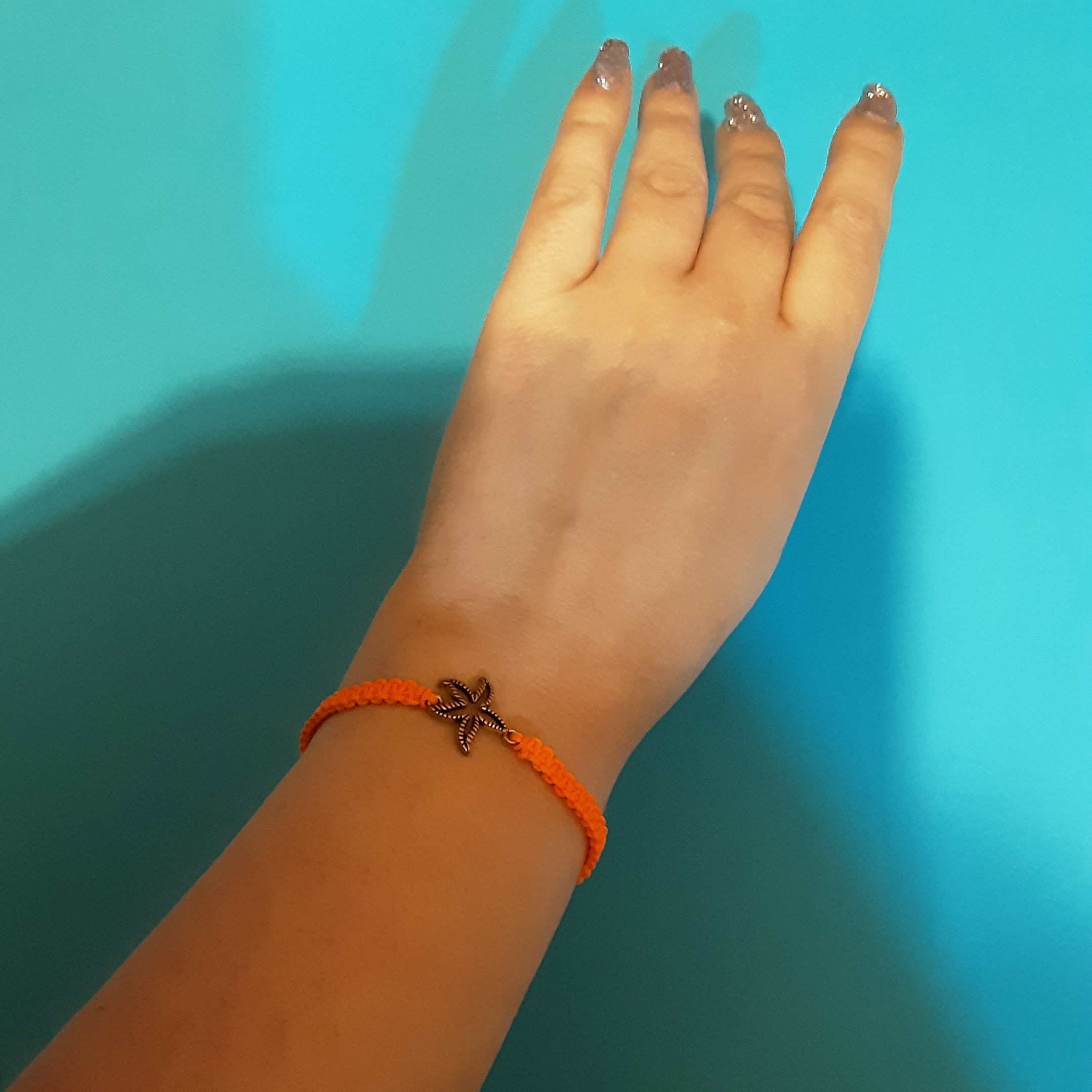 دستبند بافت.بافته شده با نخ رنگ نارنجی نئونی به همراه پلاک طرح ستاره دریایی از جنس برنج.قابل سایز