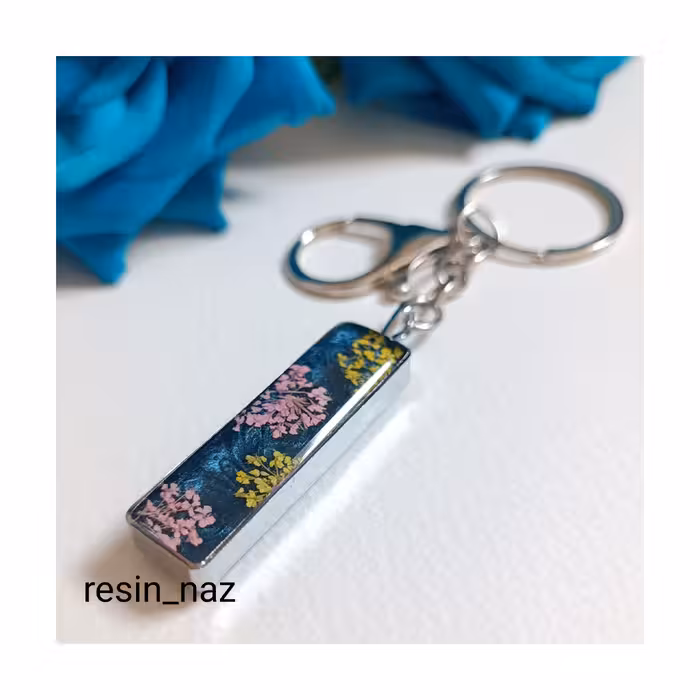 سرکلیدی و آویز کیف شیک استیل رزینی رنگ ثابت و ضدحساسیت نقره ای رنگ دوطرفه با گل شوکران و پولک صورتی شبتاب زمینه سرمه ای